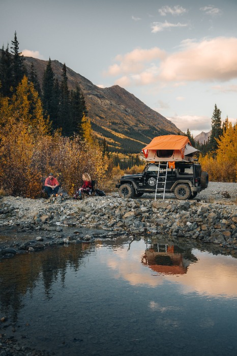 Jeep with tent on topo and two people sitting by a pond